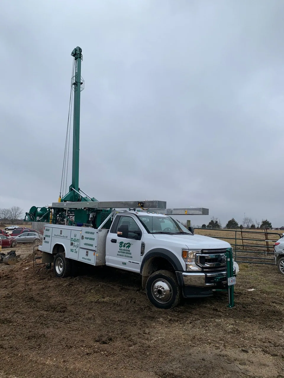 A B&H pump truck with its derrick raised over a wellhead on a rural job site