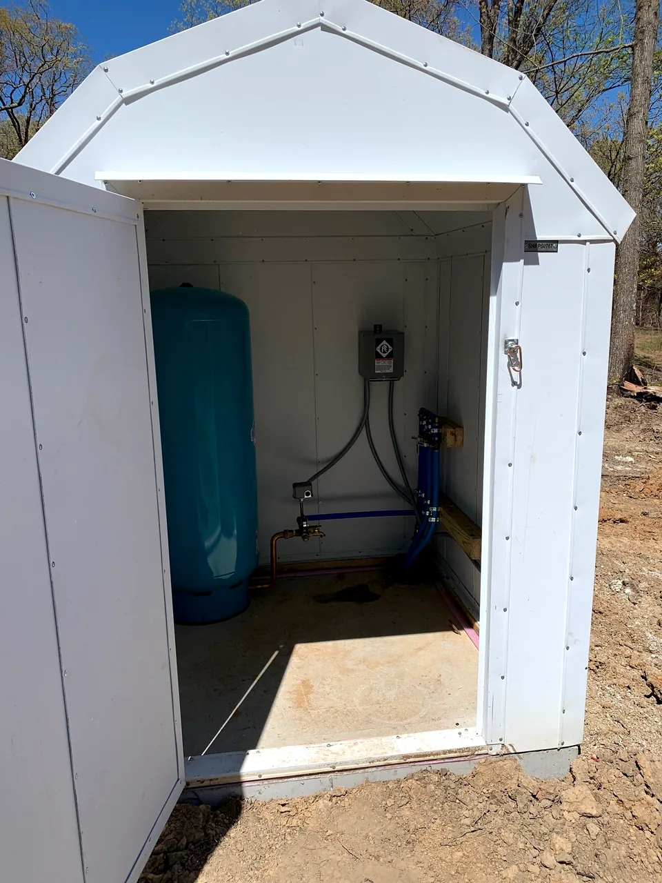 An insulated well house with the door open, showing the pressure tank and piping protected inside